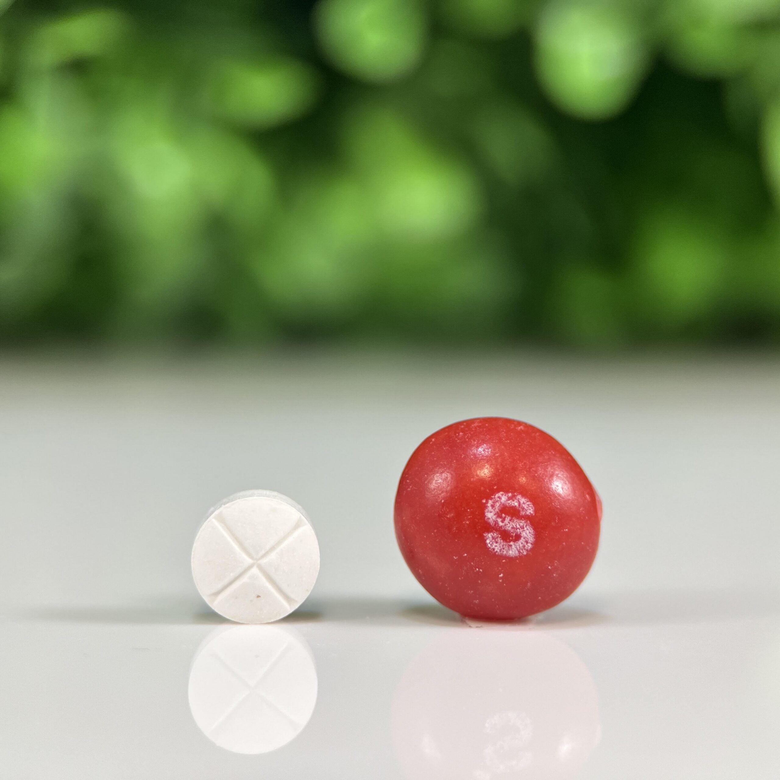 White GS-441524 quad-scored tablet compounded for cats beside a red candy for size comparison